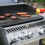 A gas grill with various foods cooking